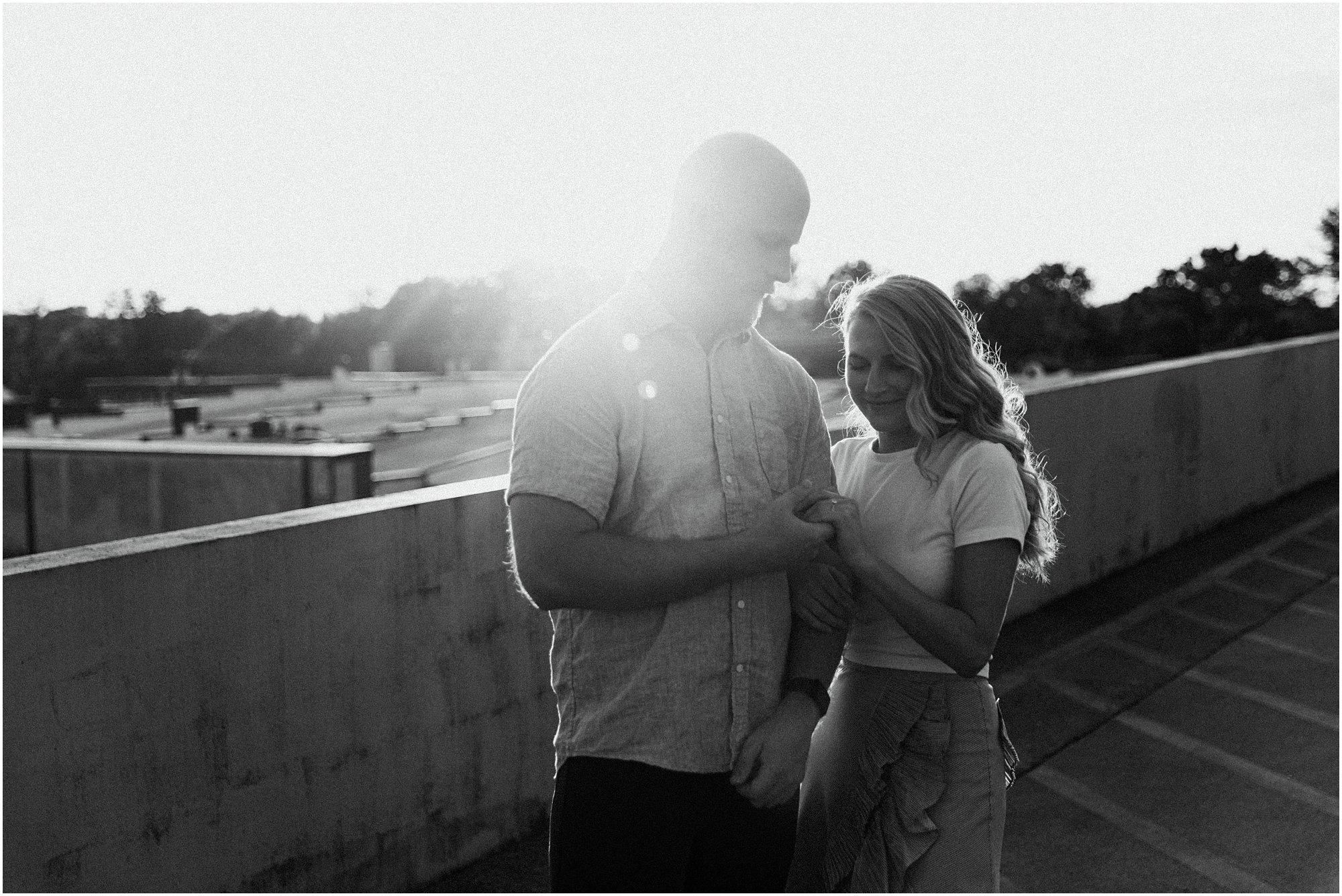 Engaged couple admiring her engagement ring on parking garage rooftop