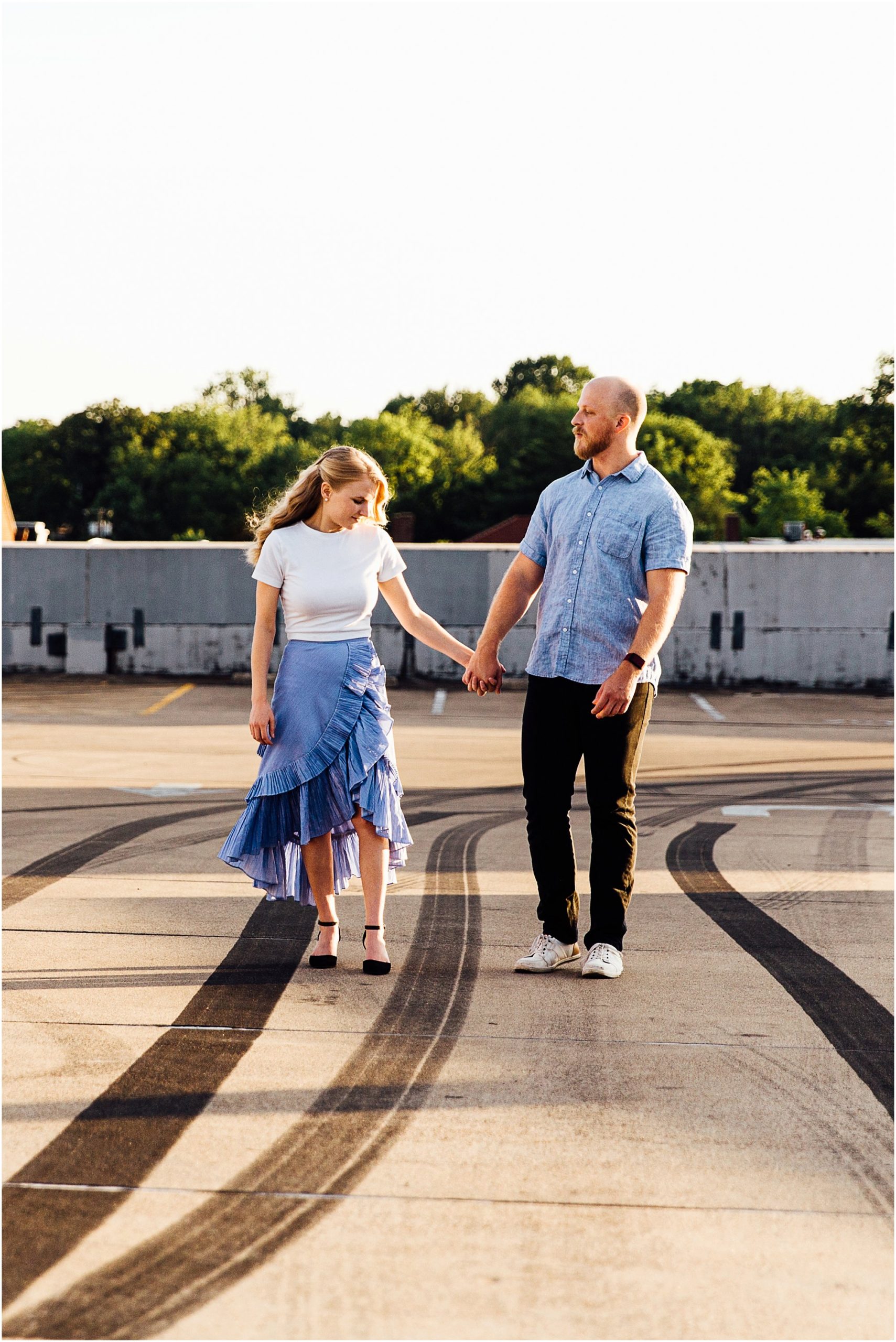 Engaged couple running on parking garage towards camera as they hold hands