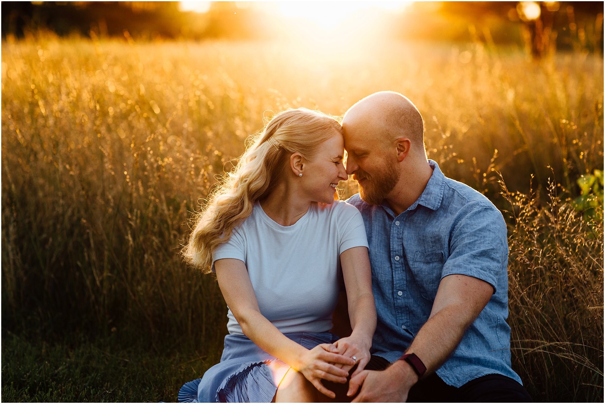 Couple touching noses and holding hands in a golden field during sunset