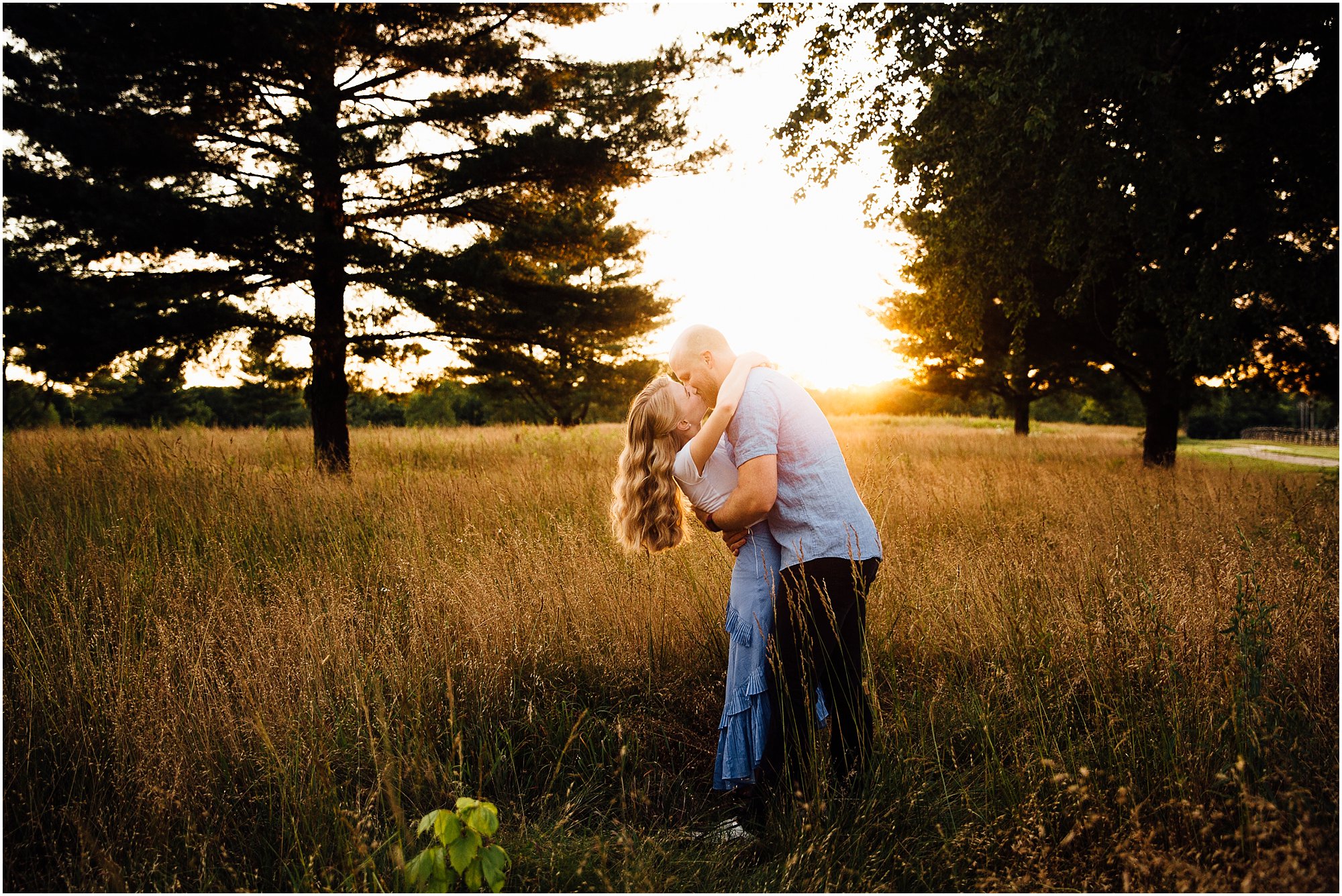 Engaged couple kissing in a golden field during sunset