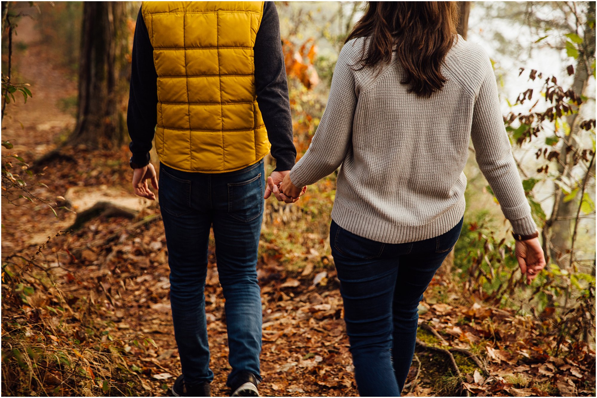 Guy and girl holding hands while hiking in amongst fall colored tress