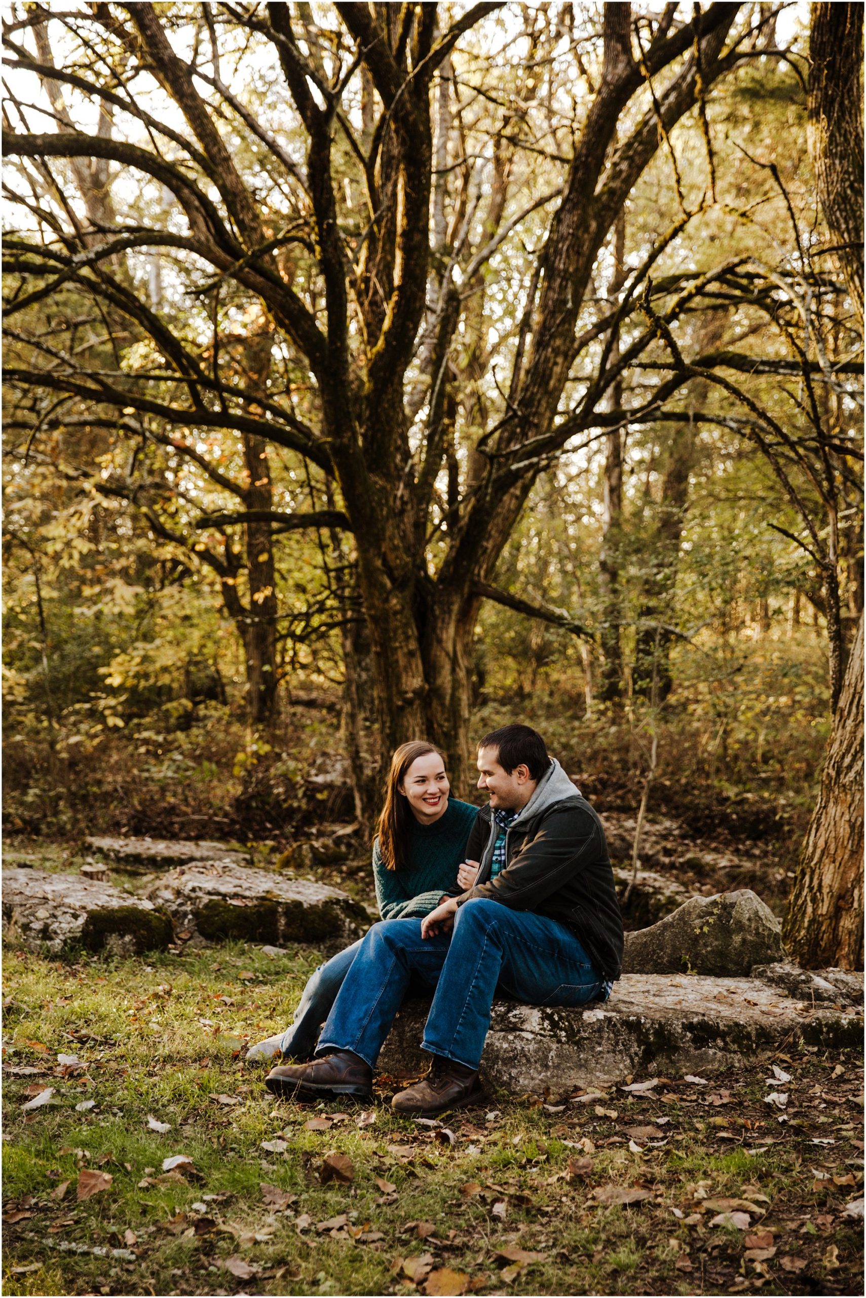 Engaged couple sitting on rock together under a tree chatting at Arrington Vineyards