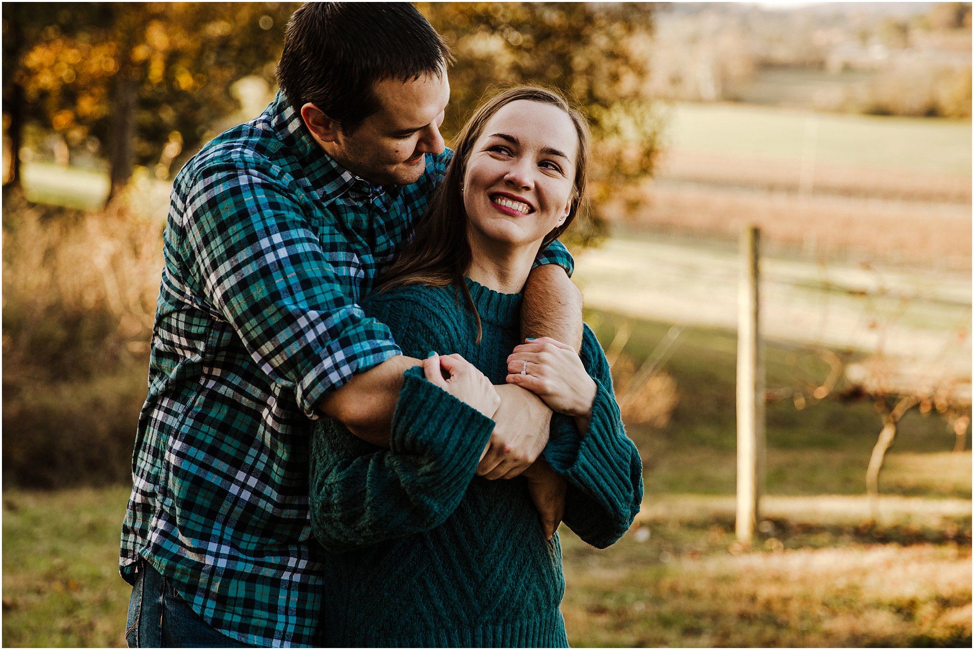 Guy bear hugging his girl as they smile on a hillside.