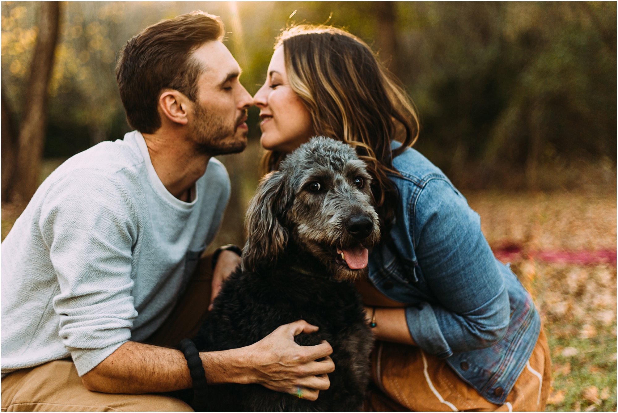 Couple going in for a kiss while their dog smiles at the camera