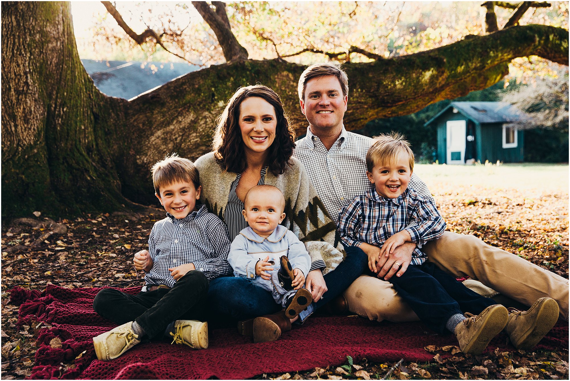 Family snuggled up smiling together on blanket under a large tree in Chattanooga, TN