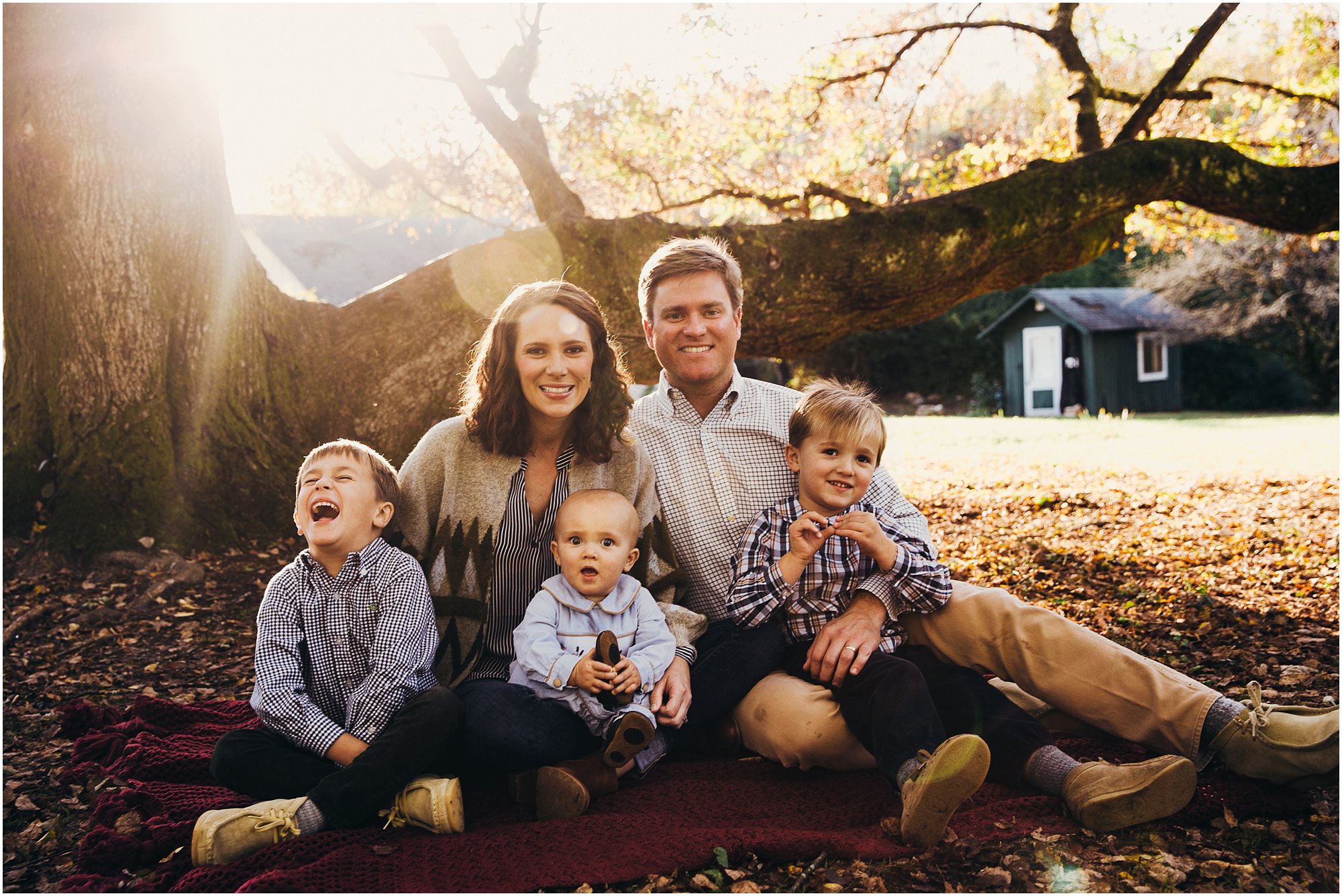 Couple with their three young boys cuddled on blanket and smiling at camera