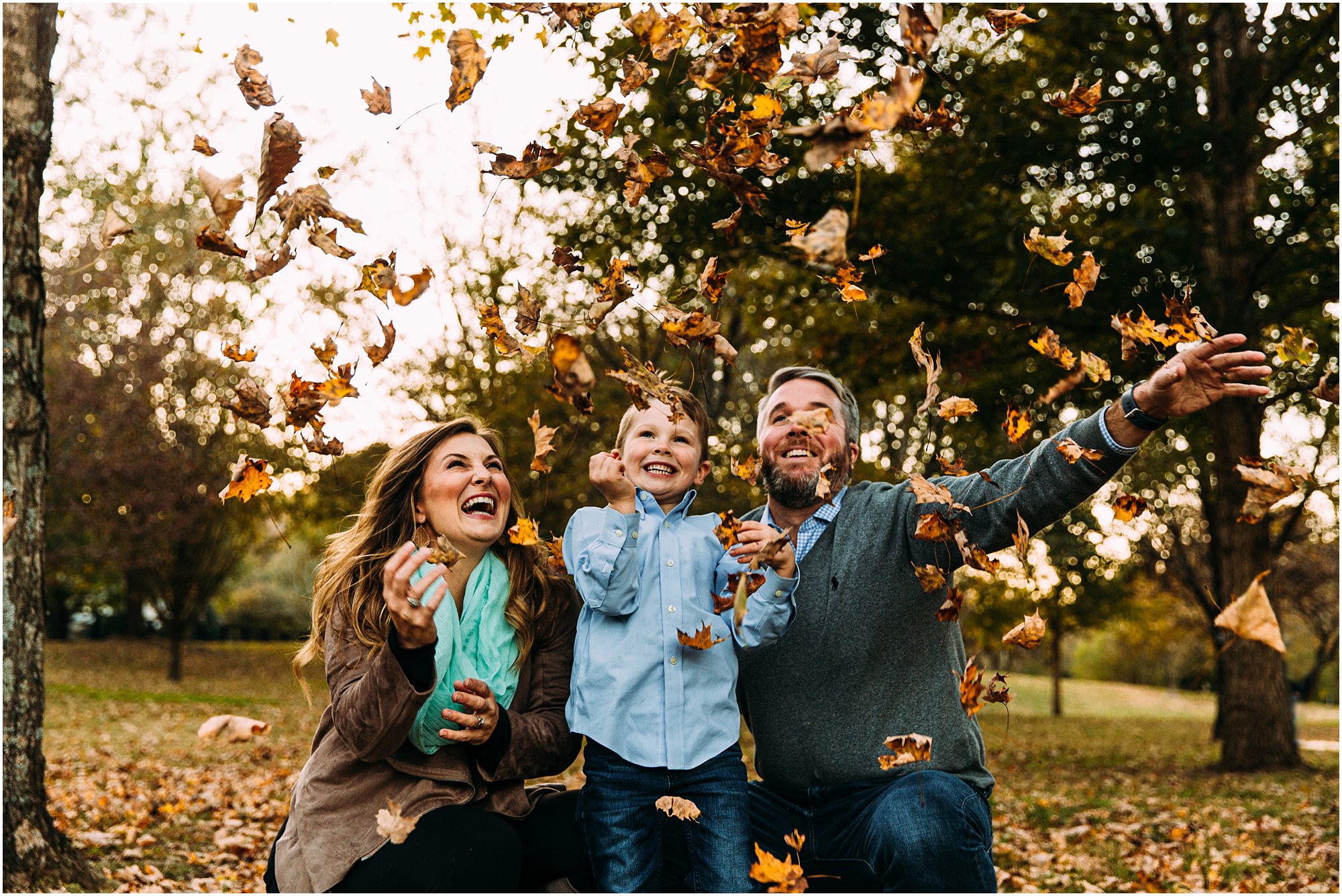 Parents and son laughing in excitement as they throw leaves into the air