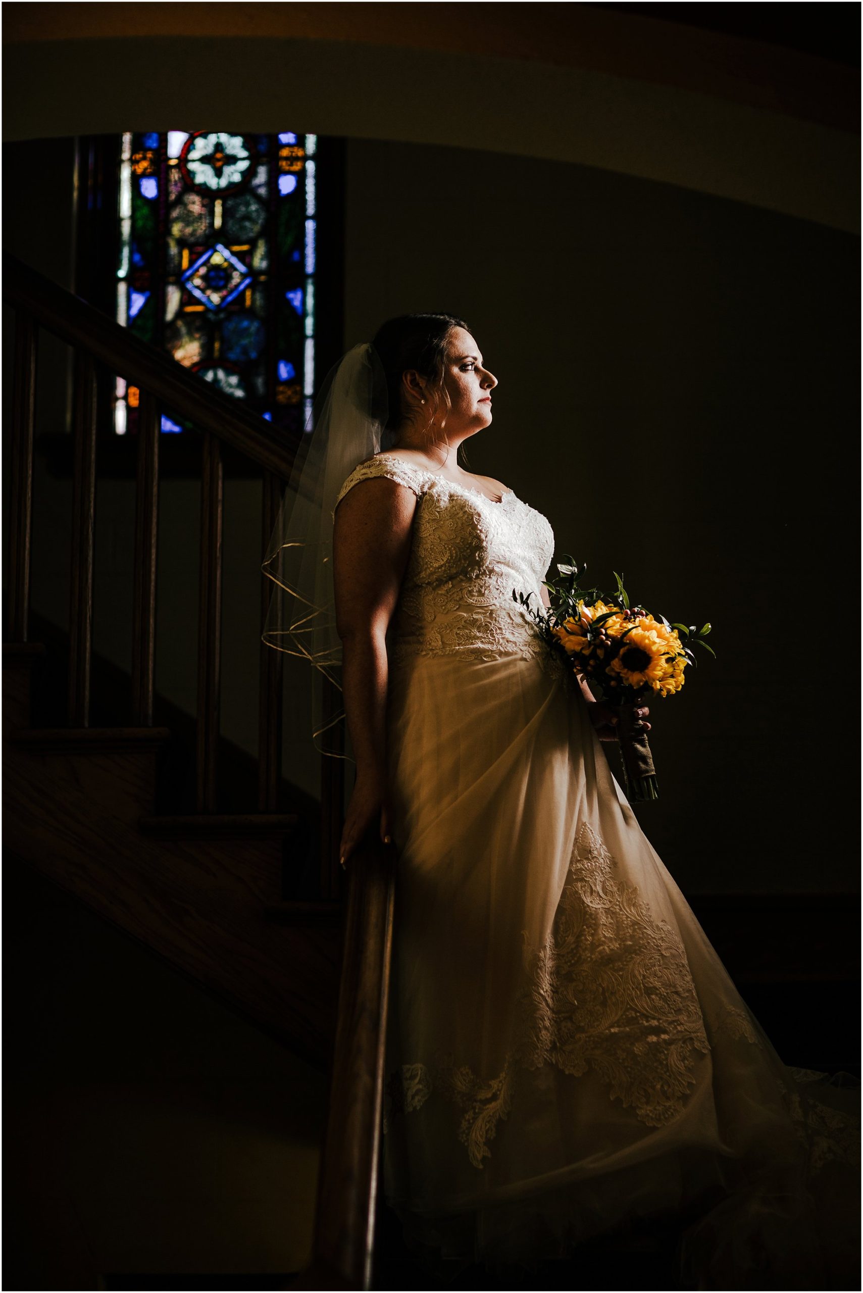 Portrait of bride on church stairs looking out window with stained glass behind her