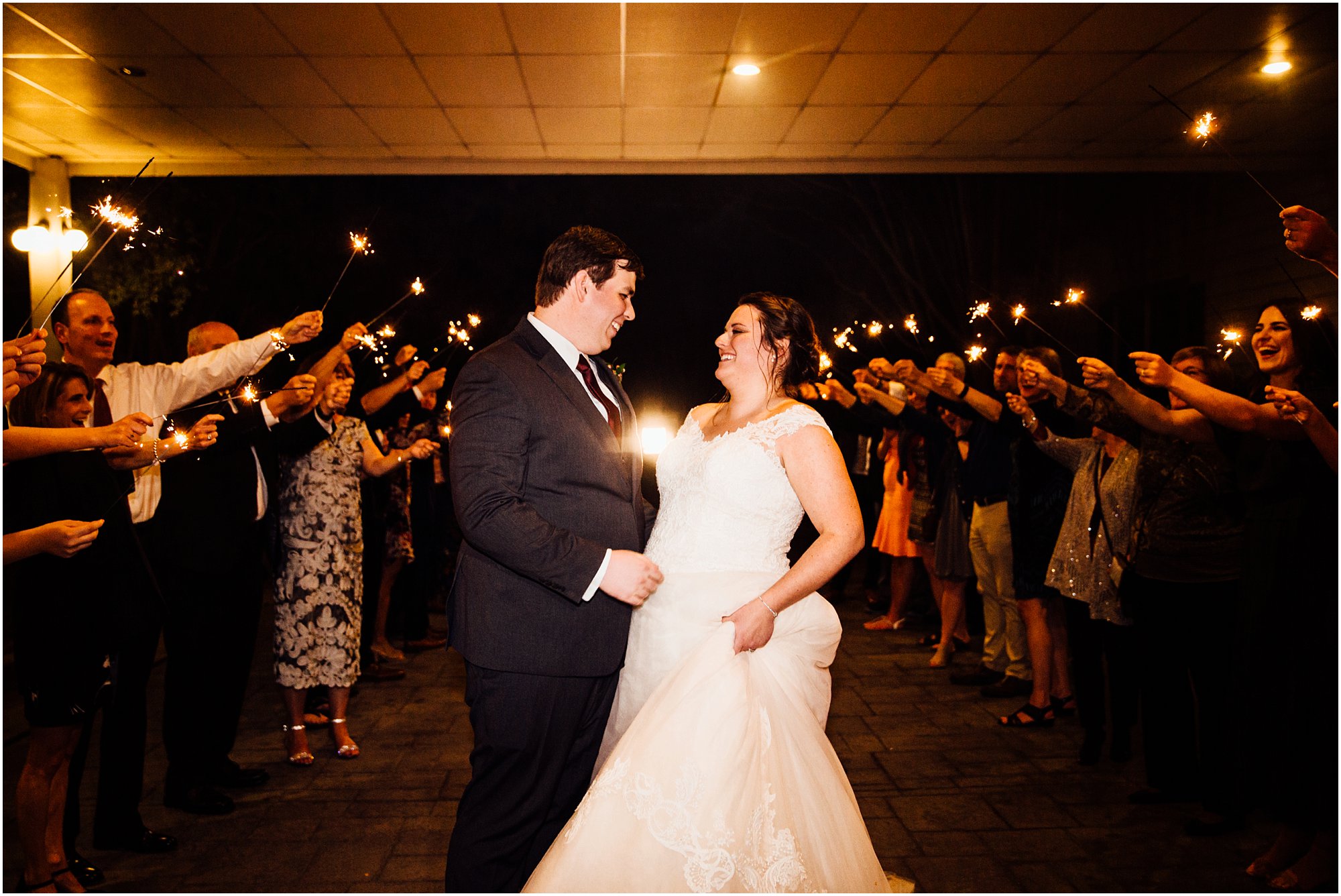 Bride and groom embracing with sparklers and guests behind them